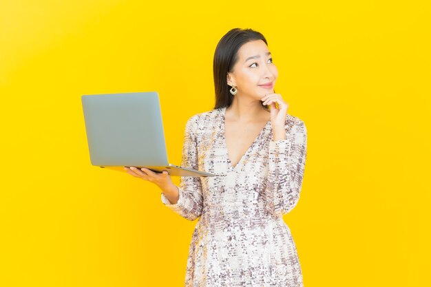 Portrait beautiful young asian woman smile with computer laptop on yellow