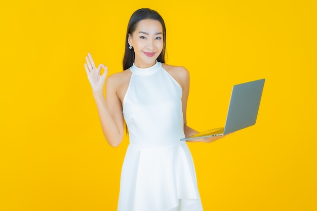 Portrait beautiful young asian woman smile with computer laptop on yellow