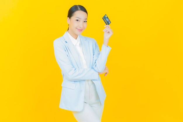 Улыбка женщины портрета красивая молодая азиатская с кредитной картой на желтом