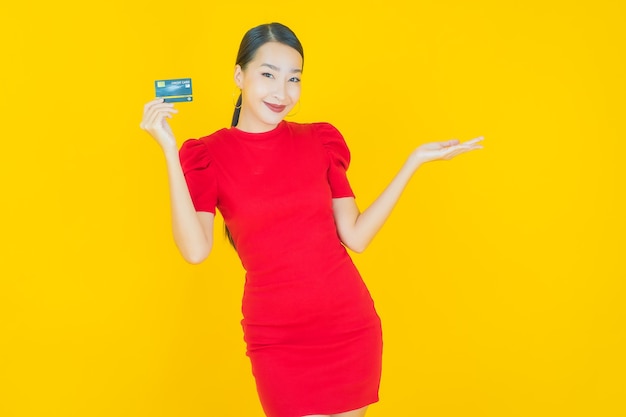 Улыбка женщины портрета красивая молодая азиатская с кредитной картой на желтом