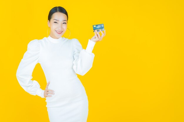 黄色のクレジットカードで笑顔美しい若いアジアの女性の肖像画