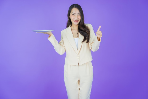Улыбка женщины портрета красивая молодая азиатская с пустой тарелкой на цветном фоне