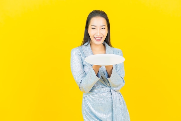 Улыбка женщины портрета красивая молодая азиатская с пустой тарелкой на желтой стене