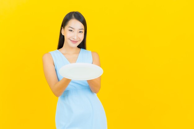 黄色の壁に空の皿皿と肖像画美しい若いアジアの女性の笑顔