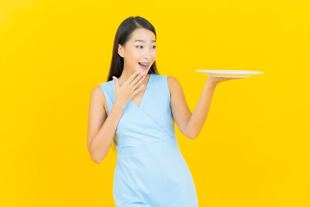 노란색 벽에 빈 접시 접시와 초상화 아름 다운 젊은 아시아 여자 미소