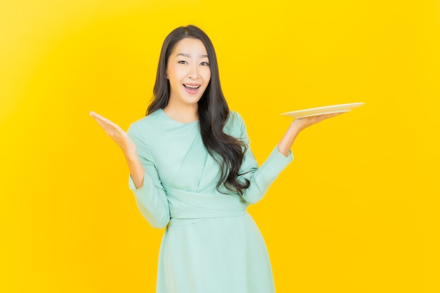 Portrait beautiful young asian woman smile with empty plate dish on yellow