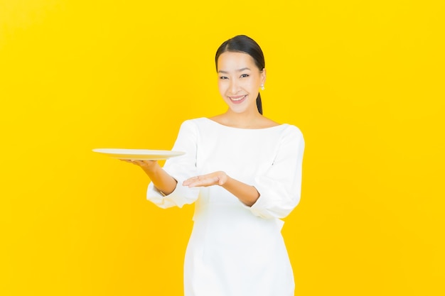 Portrait beautiful young asian woman smile with empty plate dish on yellow