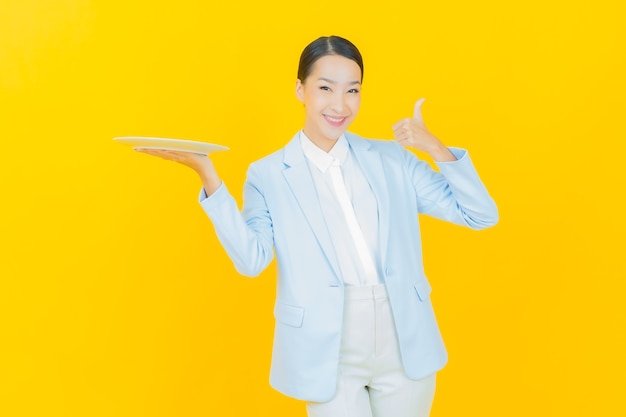 Portrait beautiful young asian woman smile with empty plate dish on yellow