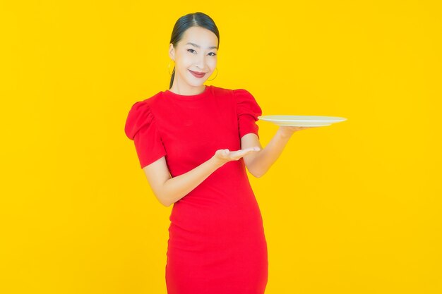 Portrait beautiful young asian woman smile with empty plate dish on yellow