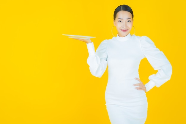 Portrait beautiful young asian woman smile with empty plate dish on yellow