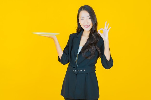 Portrait beautiful young asian woman smile with empty plate dish on yellow