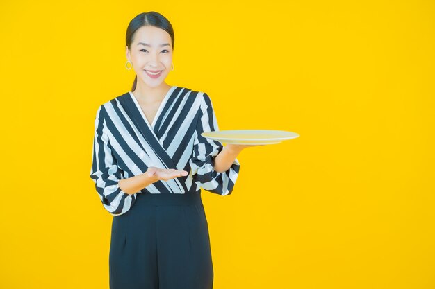 Portrait beautiful young asian woman smile with empty plate dish on yellow