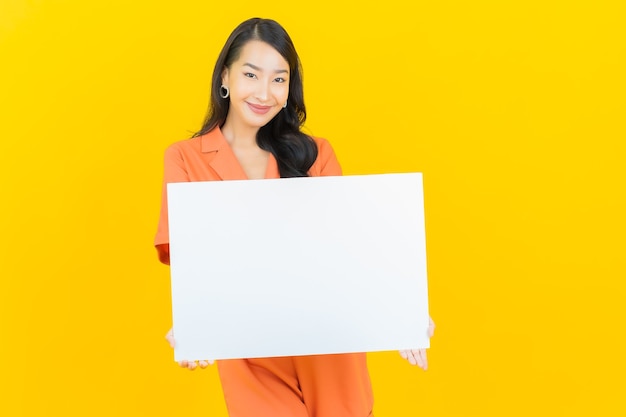 Portrait beautiful young asian woman smile with empty white billboard on yellow