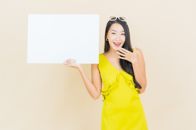 Улыбка женщины портрета красивая молодая азиатская с пустой белой доской на желтой стене