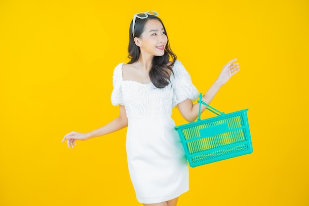 노란색 슈퍼마켓에서 식료품 바구니를 들고 웃는 아름다운 젊은 아시아 여성