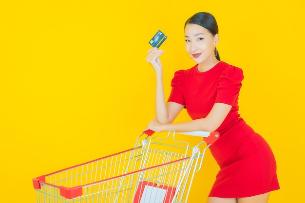 Улыбка женщины портрета красивая молодая азиатская с продуктовой корзиной из супермаркета на желтом