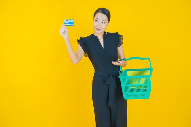 Portrait beautiful young asian woman smile with grocery basket from supermarket on on yellow