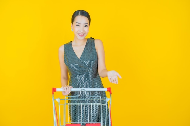 Free photo portrait beautiful young asian woman smile with grocery basket from supermarket on yellow