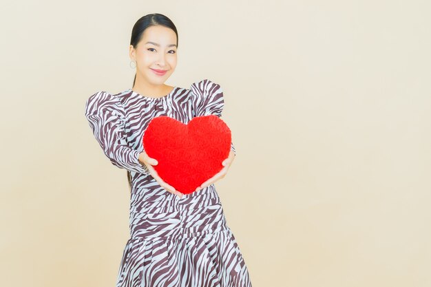 Улыбка женщины портрета красивая молодая азиатская с формой подушки сердца на бежевом