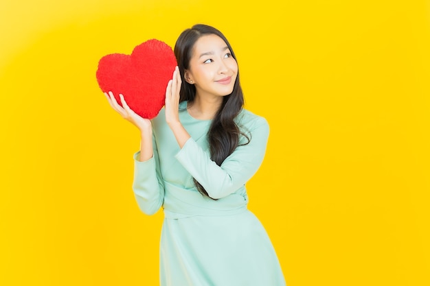 Улыбка женщины портрета красивая молодая азиатская с формой подушки сердца на желтом