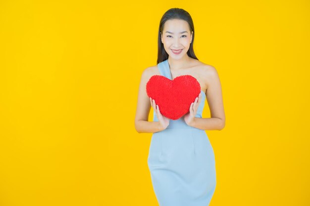 Portrait beautiful young asian woman smile with heart pillow shape on yellow