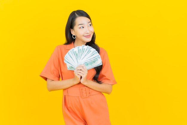 Portrait beautiful young asian woman smile with a lot of cash and money on yellow