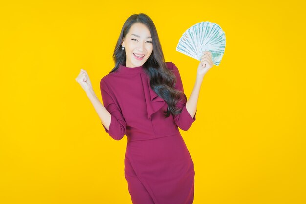 Portrait beautiful young asian woman smile with a lot of cash and money on yellow