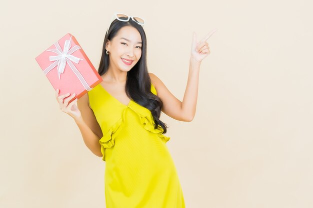Portrait beautiful young asian woman smile with red gift box on color wall
