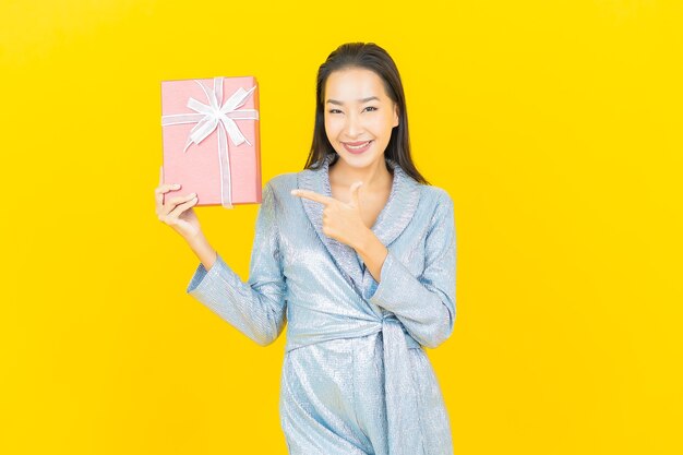 노란색 벽에 빨간색 선물 상자와 세로 아름 다운 젊은 아시아 여자 미소