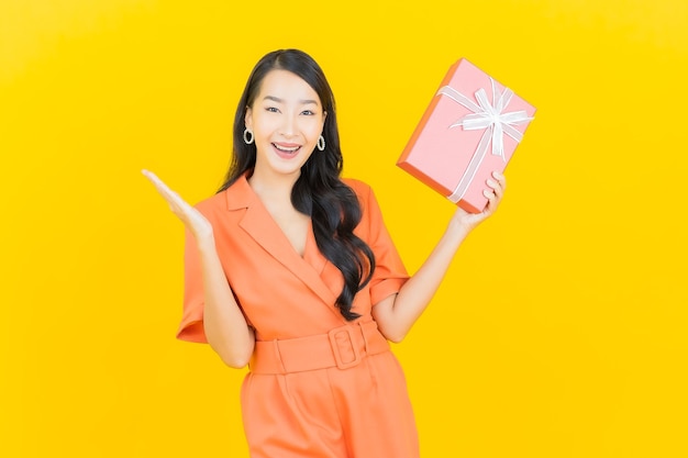 Portrait beautiful young asian woman smile with red gift box on yellow