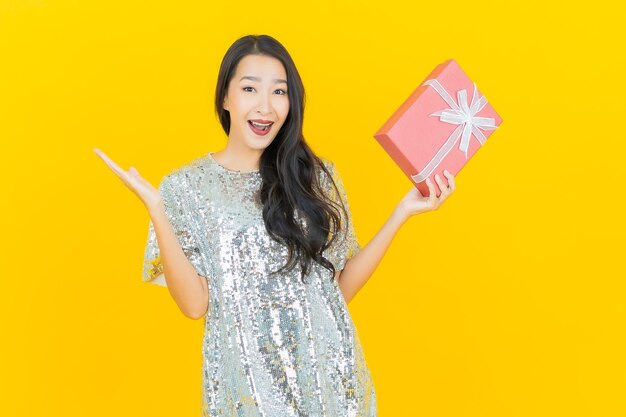 Portrait beautiful young asian woman smile with red gift box on yellow