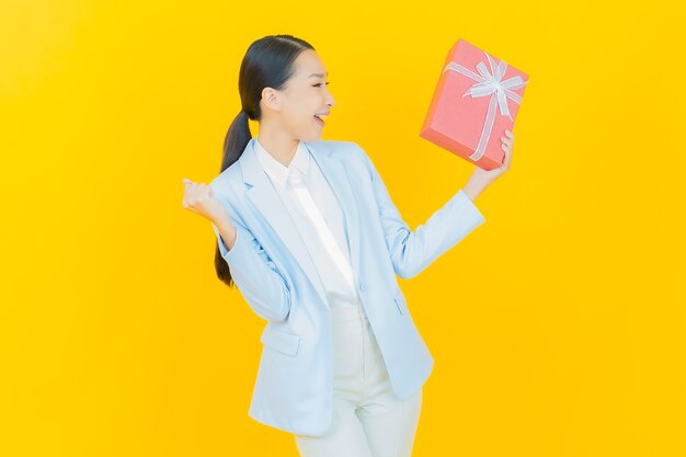 Portrait beautiful young asian woman smile with red gift box on yellow