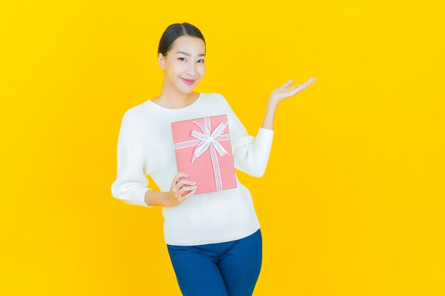 Portrait beautiful young asian woman smile with red gift box on yellow