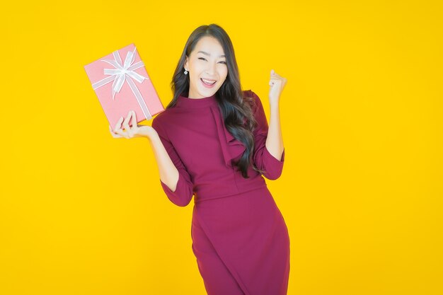 Portrait beautiful young asian woman smile with red gift box on yellow