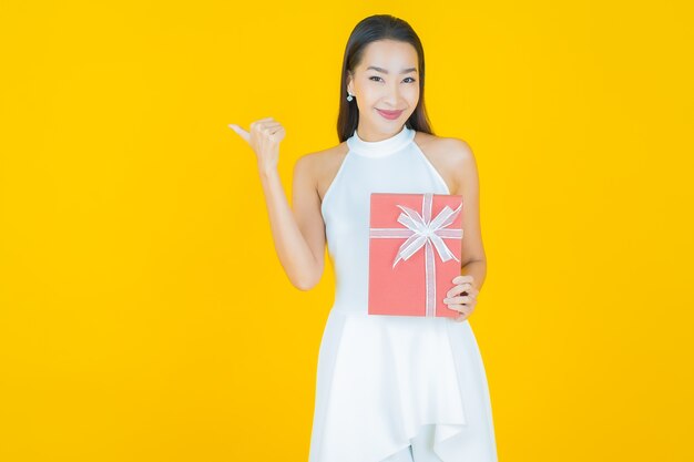 Portrait beautiful young asian woman smile with red gift box on yellow