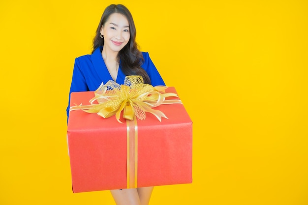 Portrait beautiful young asian woman smile with red gift box on yellow