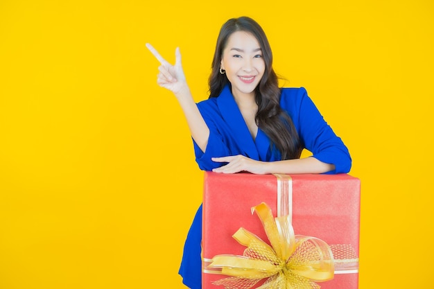 Portrait beautiful young asian woman smile with red gift box on yellow