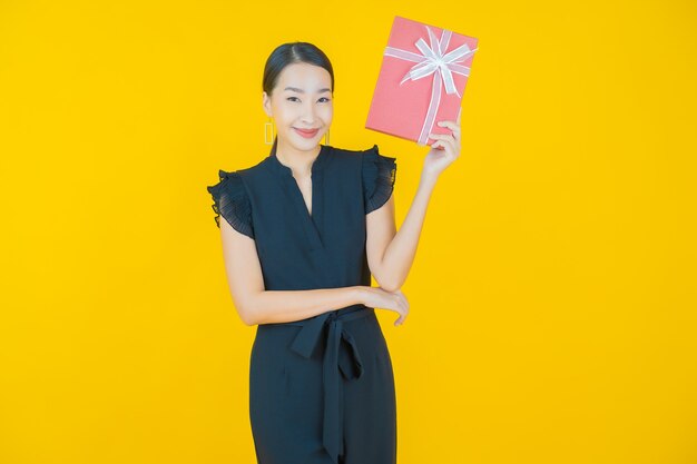 Portrait beautiful young asian woman smile with red gift box on on yellow