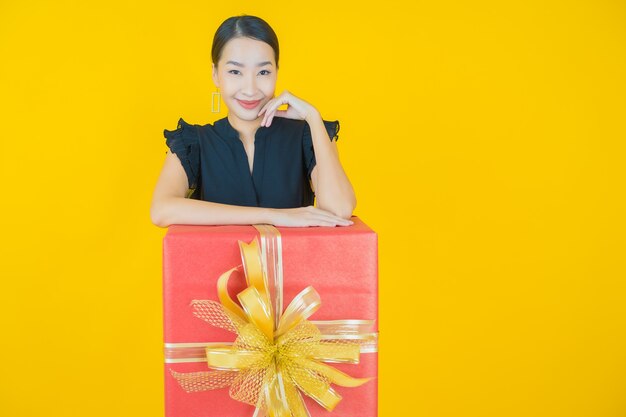 Portrait beautiful young asian woman smile with red gift box on on yellow