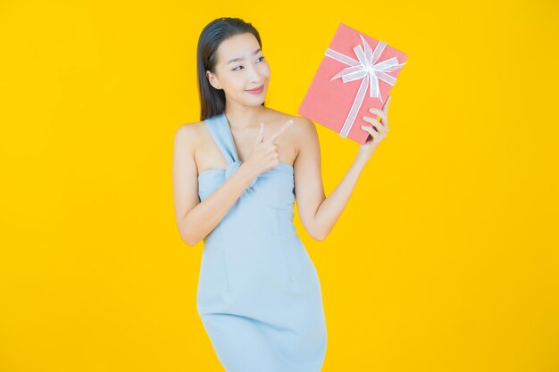 Portrait beautiful young asian woman smile with red gift box on yellow