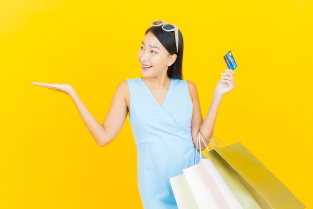 Portrait beautiful young asian woman smile with shopping bag on yellow color wall