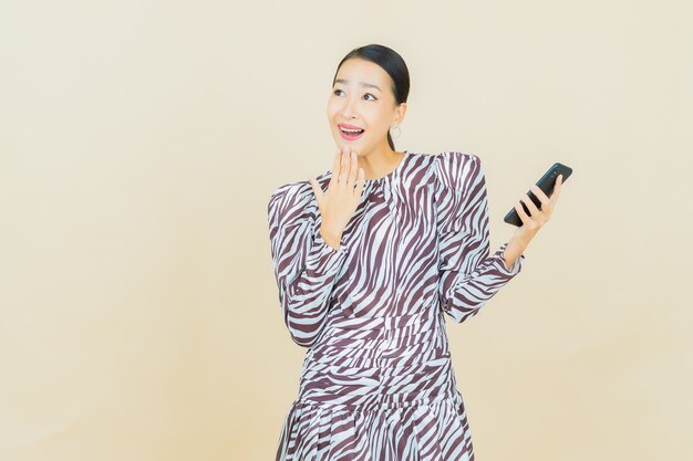Sorriso di bella giovane donna asiatica del ritratto con il telefono cellulare astuto su beige