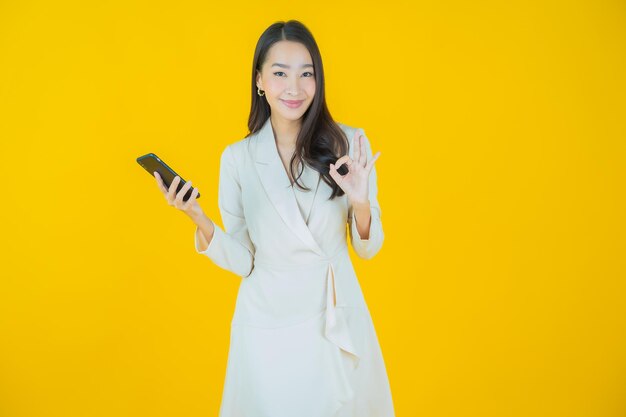 肖像画美しい若いアジアの女性は、色の背景にスマート携帯電話で笑顔