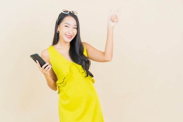色の壁にスマート携帯電話で笑顔美しい若いアジアの女性