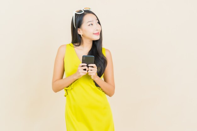 色の壁にスマート携帯電話で笑顔美しい若いアジアの女性