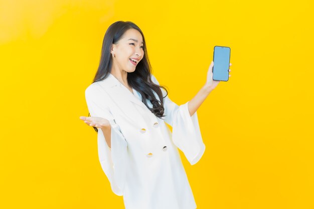 黄色の壁にスマートな携帯電話で笑顔の美しい若いアジアの女性の肖像画