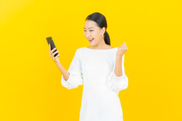 黄色のスマート携帯電話で笑顔美しい若いアジアの女性の肖像画