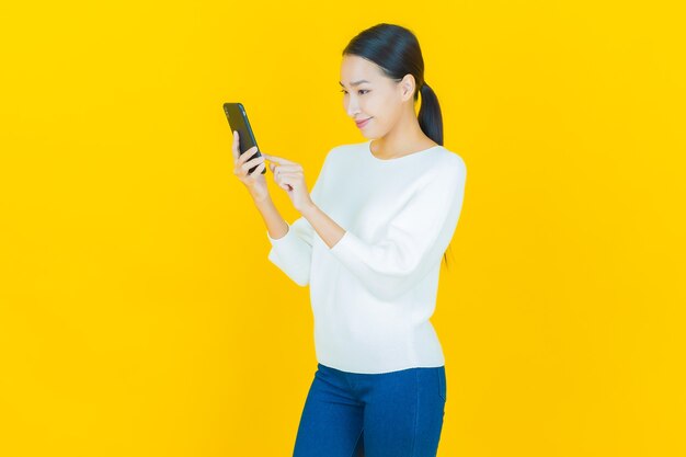 黄色のスマート携帯電話で笑顔美しい若いアジアの女性の肖像画