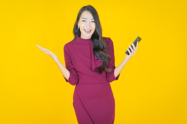 Улыбка женщины портрета красивая молодая азиатская с умным мобильным телефоном на желтом цвете