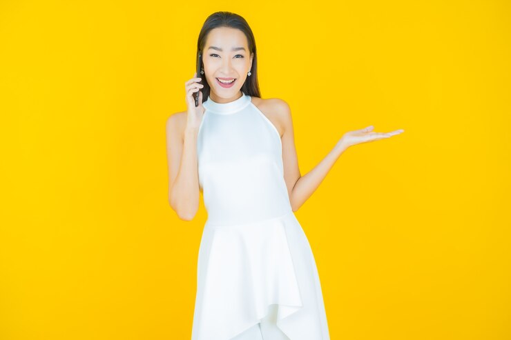無料Photo 黄色のスマート携帯電話で笑顔美しい若いアジアの女性の肖像画